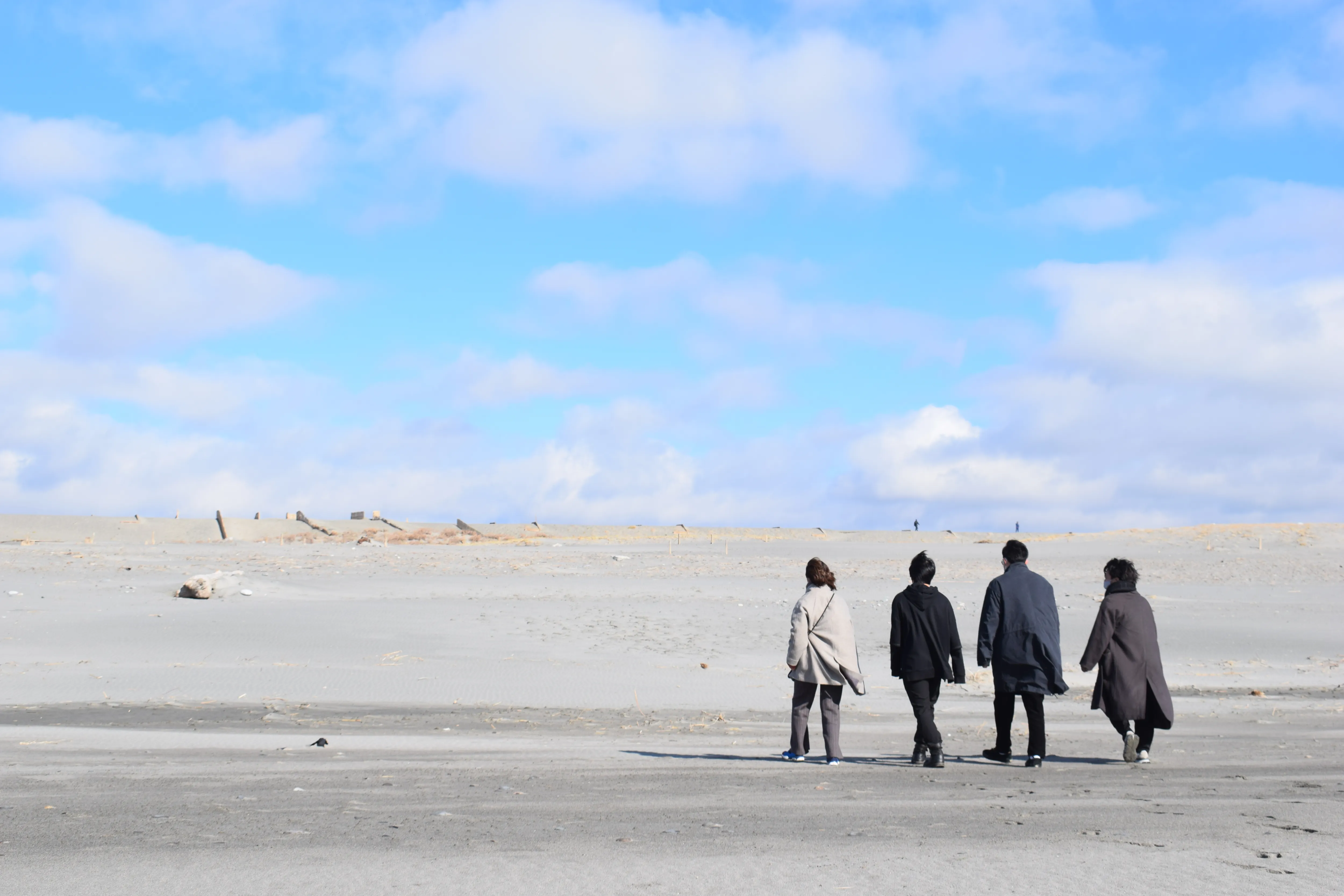 砂浜を歩く四人の若者の写真